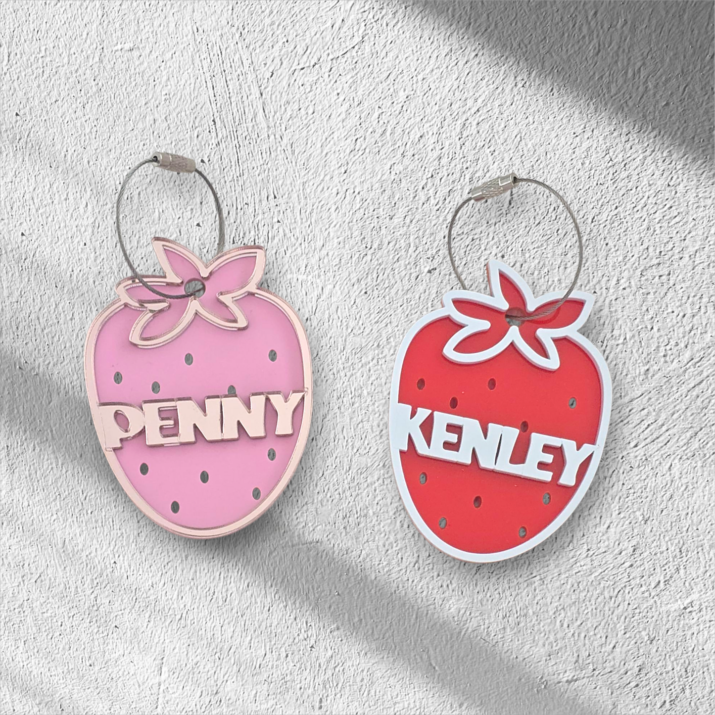 Two strawberry-shaped keychains with 'Penny' and 'Kenley' text on a light gray background
