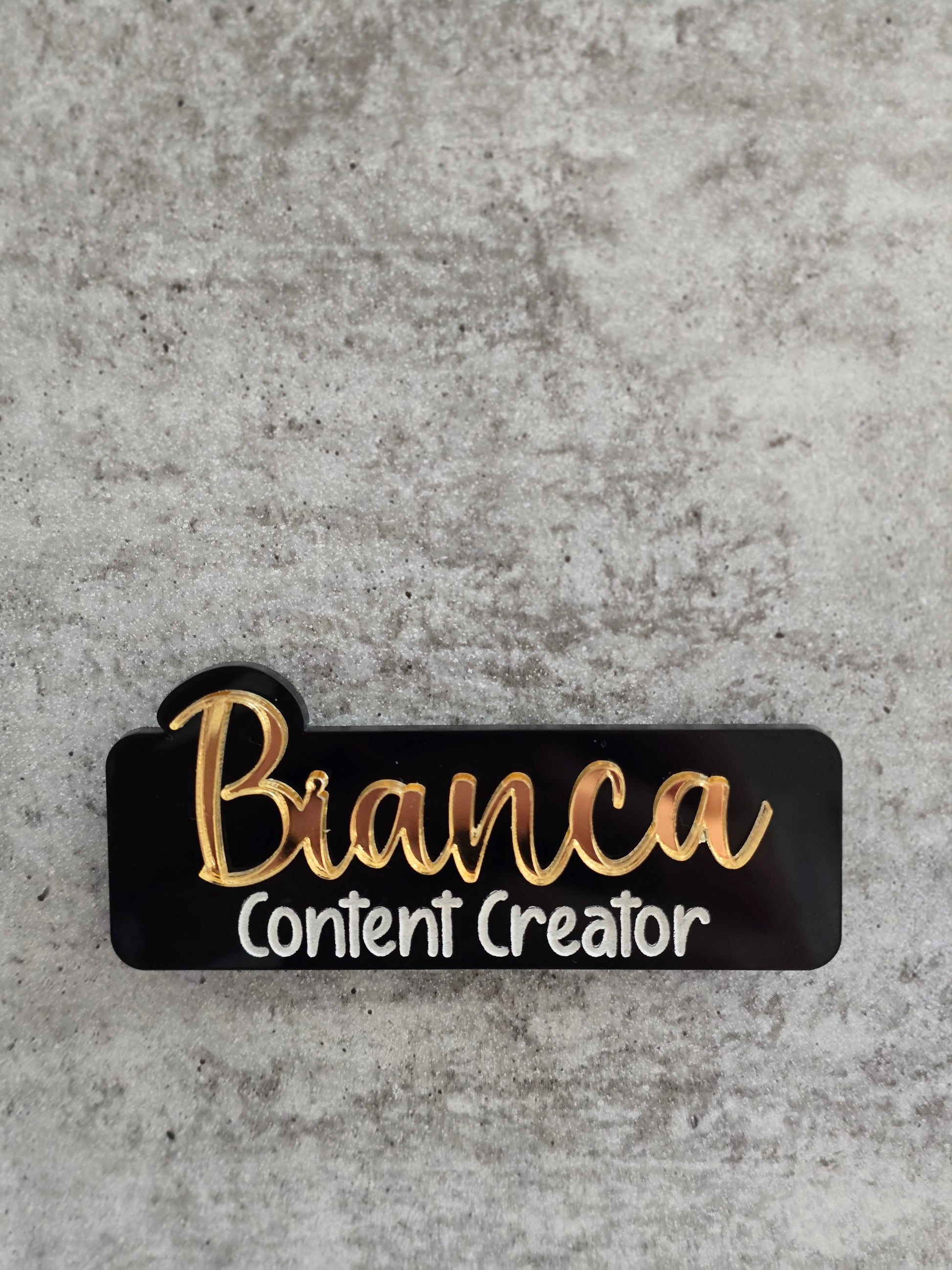 Black name tag with gold text 'Bianca Content Creator' on a concrete background
